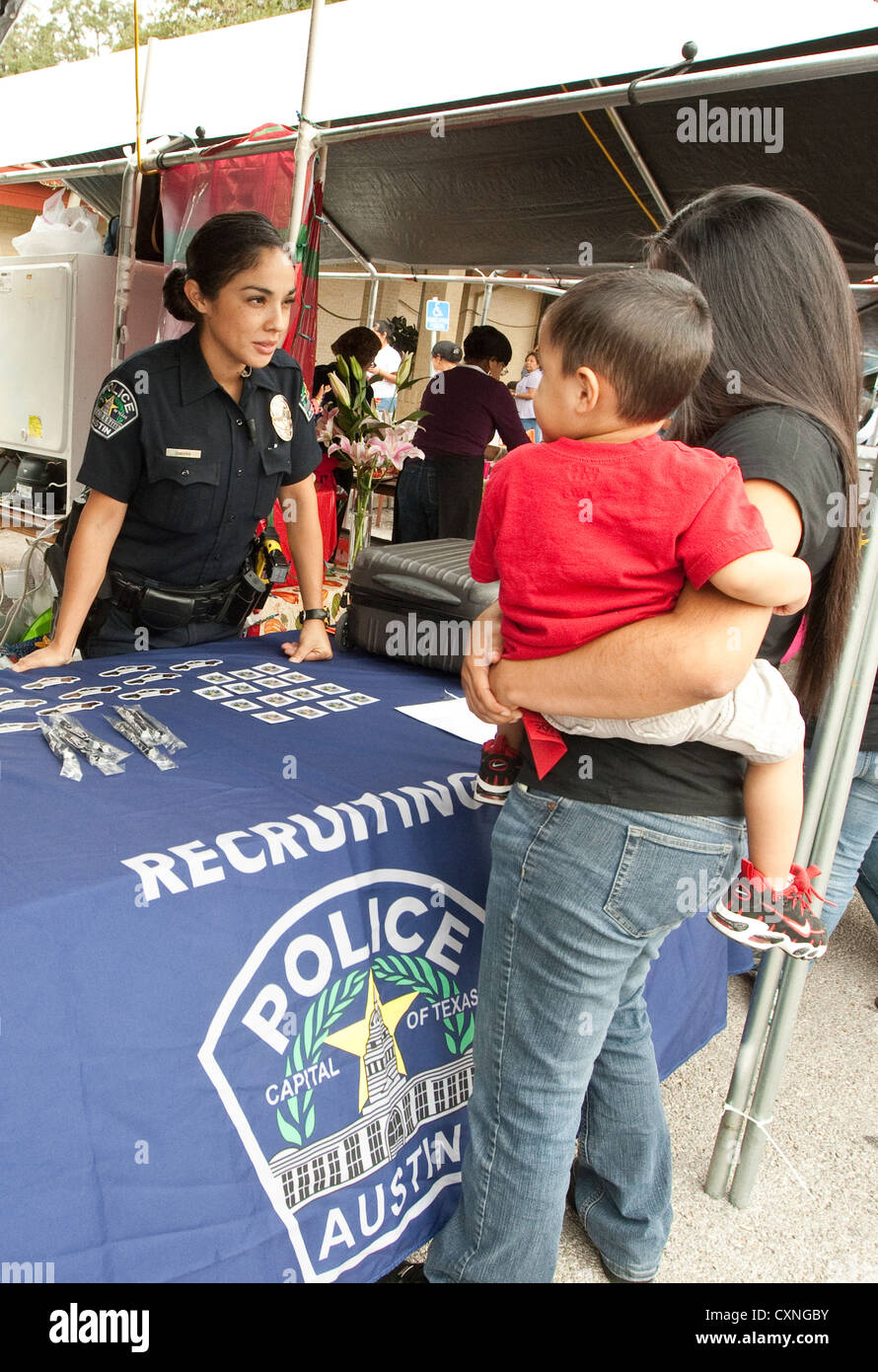 Hispanic female police officer speaks to woman carrying young son at