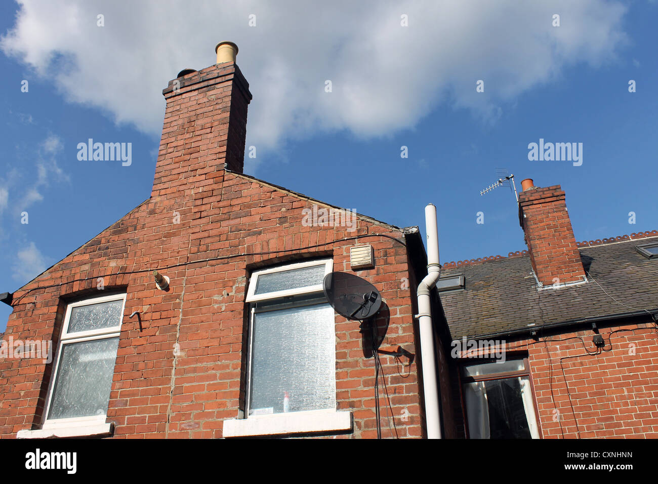 Old brick house or home with chimney and satellite dish, blue sky and cloudscape background. Stock Photo