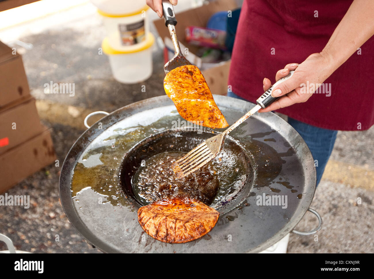Hispanic woman prepares traditional Mexican enchiladas by passing corn tortilla through hot oil sauce at outdoor church festival Stock Photo