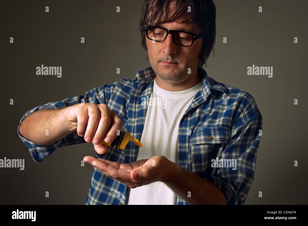 Casual young adult man shaking out painkiller pills into his hand, healthcare and medicine concept. Stock Photo