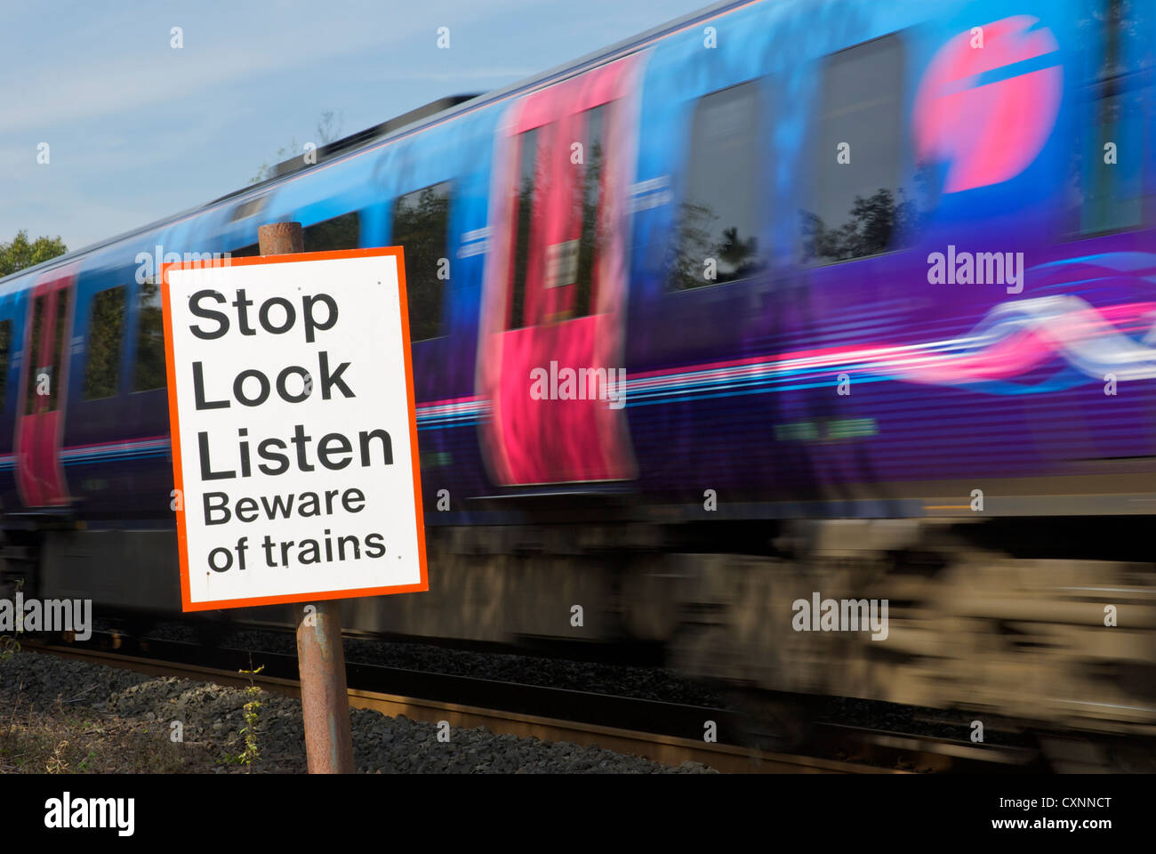 Speeding train and sign, by pedestrian crossing over railway line, warning people about trains Stock Photo