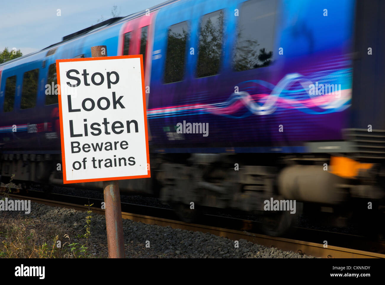 Speeding train and sign, by pedestrian crossing over railway line, warning people about trains Stock Photo