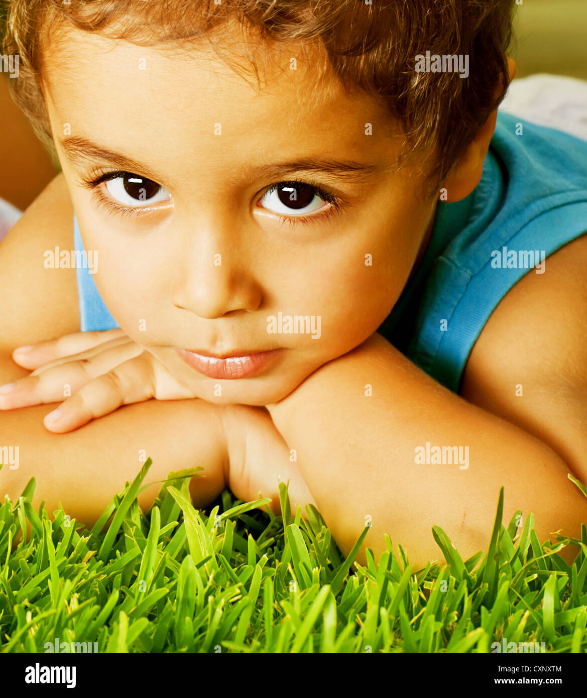 Photo of cute little serious boy lying down on fresh green grass