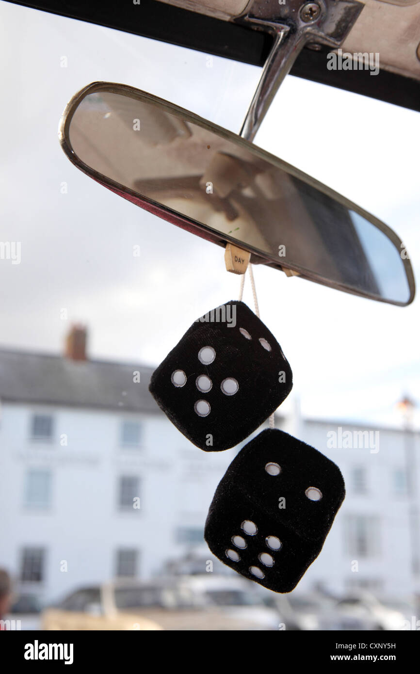 Black and white furry fuzzy dice hanging from rear view mirror, showing exterior view through windscreen of classic, Suffolk, UK Stock Photo