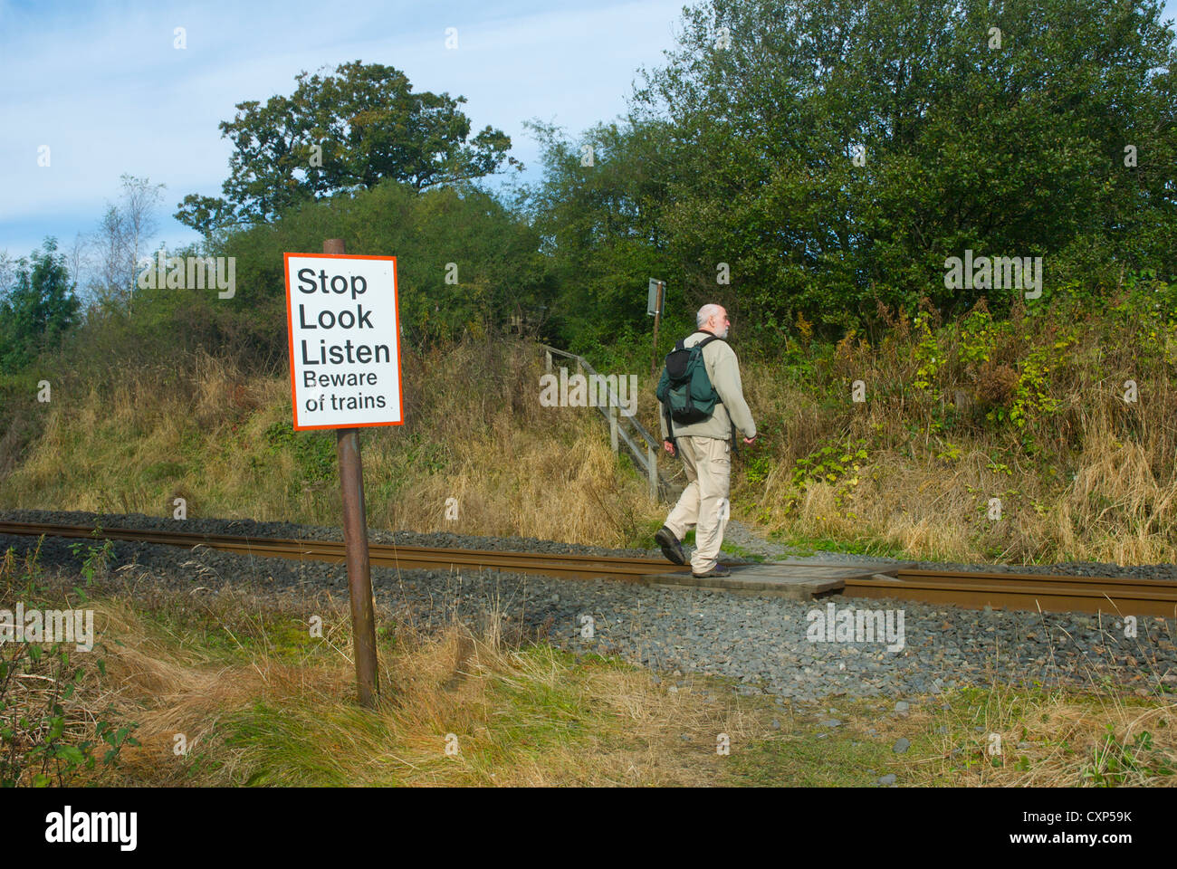 Man walking across railway line, with sign warning about the danger of trains Stock Photo