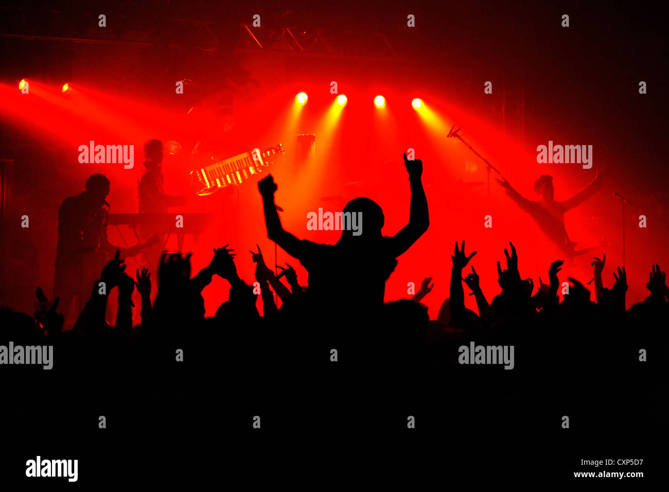 Silhouetted spectators / crowd and ambiance during live rock concert with rockers on stage illuminated by red spotlights Stock Photo