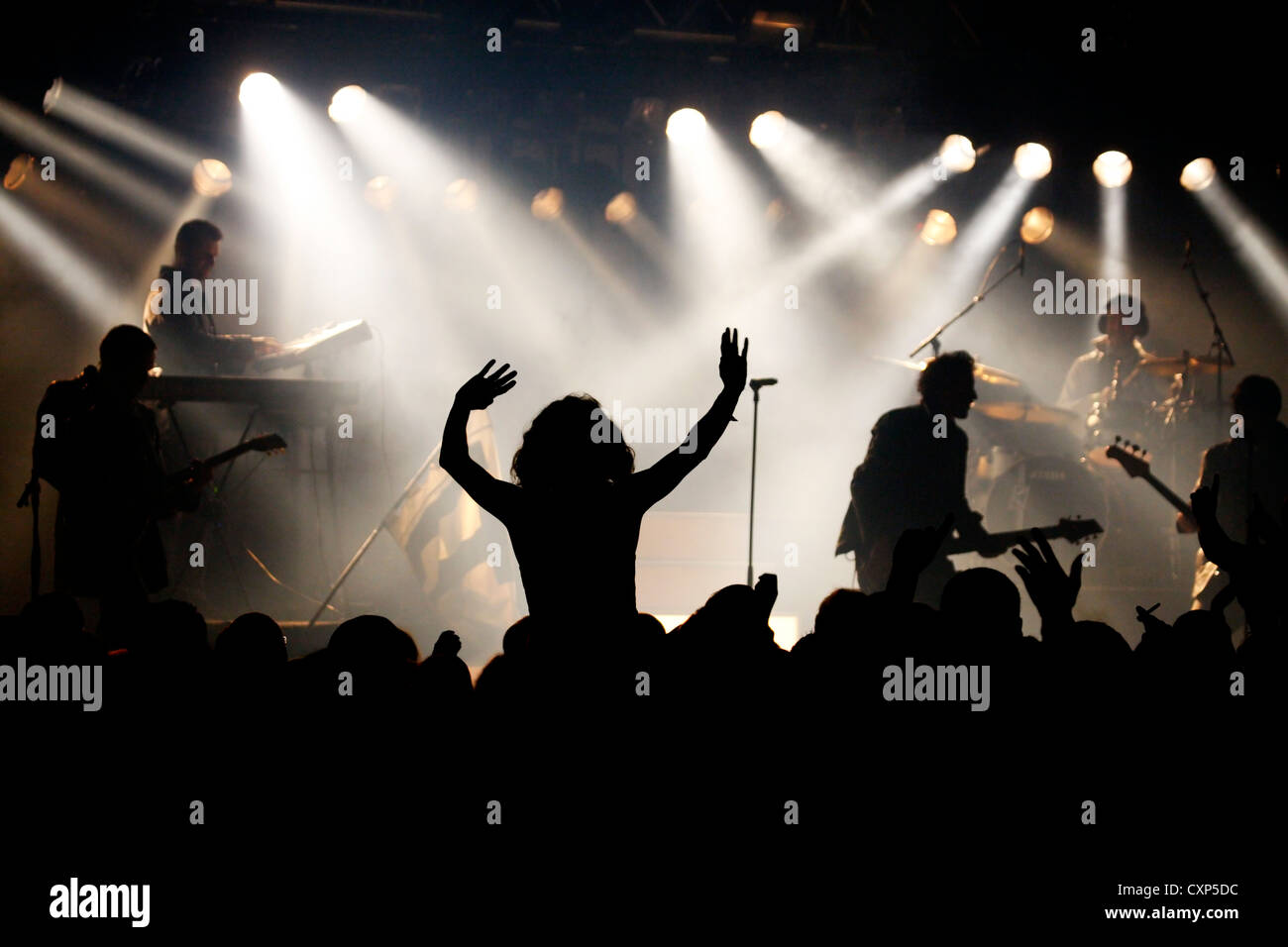 Silhouetted spectators / crowd and ambiance during live rock concert with rockers on stage illuminated by spotlights Stock Photo