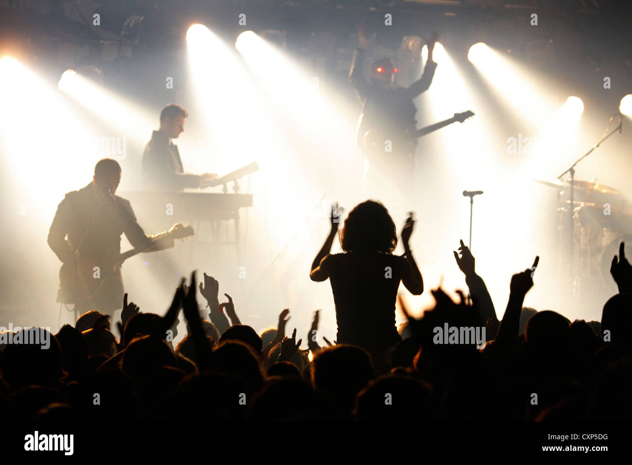 Silhouetted spectators / crowd and ambiance during live rock concert with rockers on stage illuminated by spotlights Stock Photo