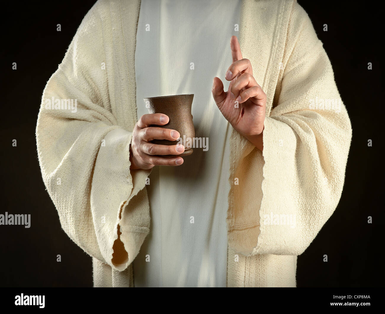 Jesus hands holding cup of wine isolated over dark background Stock Photo