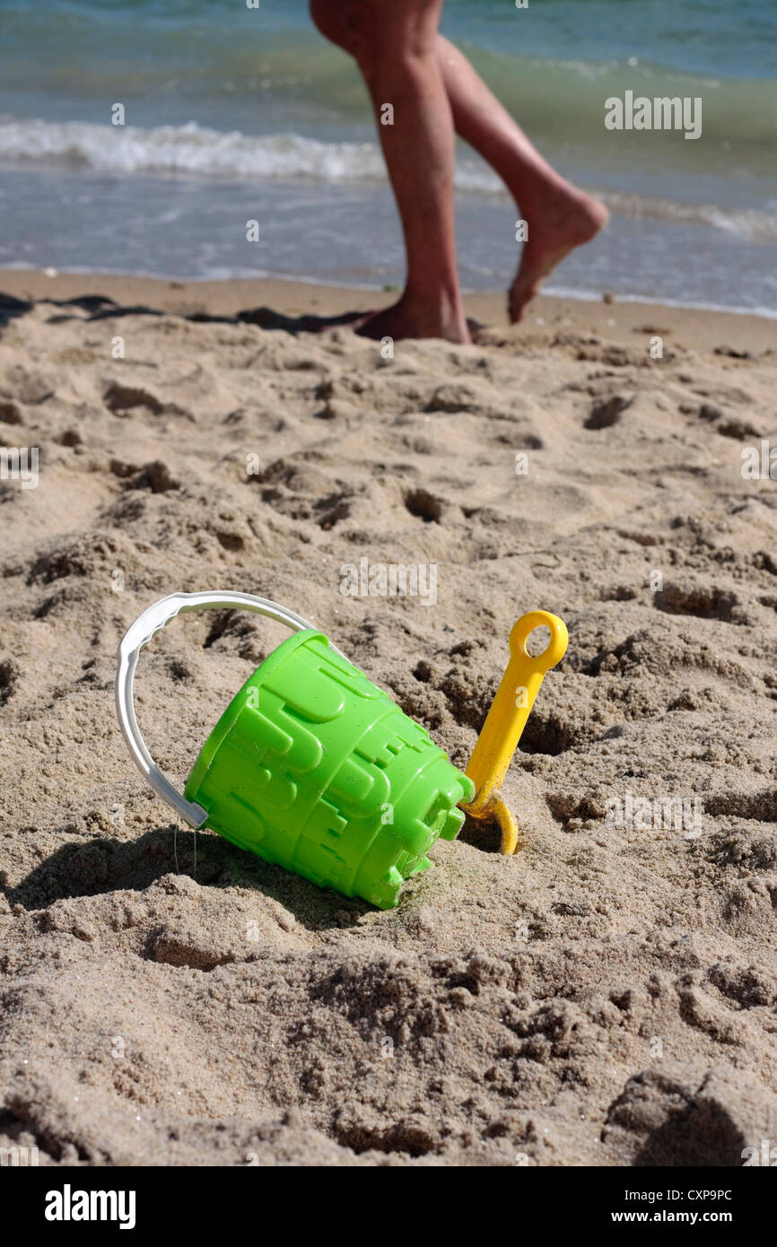 Bucket and spade on beach with person walking past Stock Photo