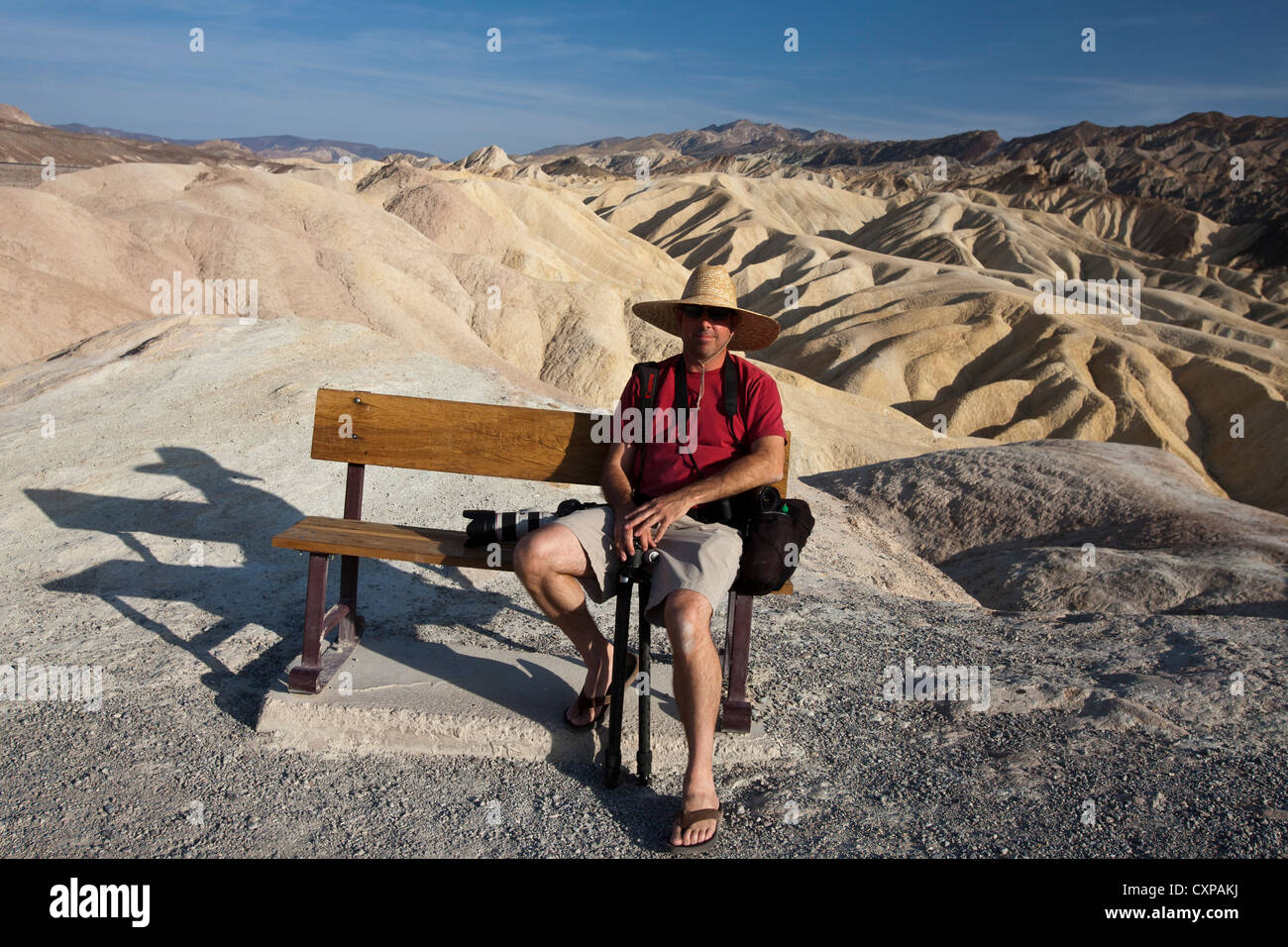 Adult male sits on park bench in front badlands Zabriskie Point Death Valley National Park California United States America Stock Photo