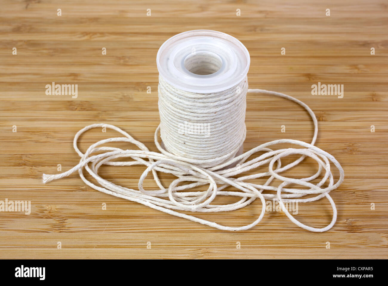 Close view of a roll of butcher's cotton twine used for cooking on a wood cutting board. Stock Photo