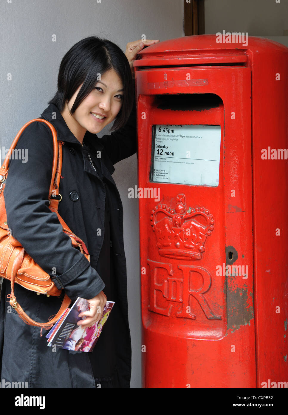 Young Japanese woman posting letters in traditional red Royal Mail letterbox, Stratford upon Avon, Warwickshire, England, UK Stock Photo