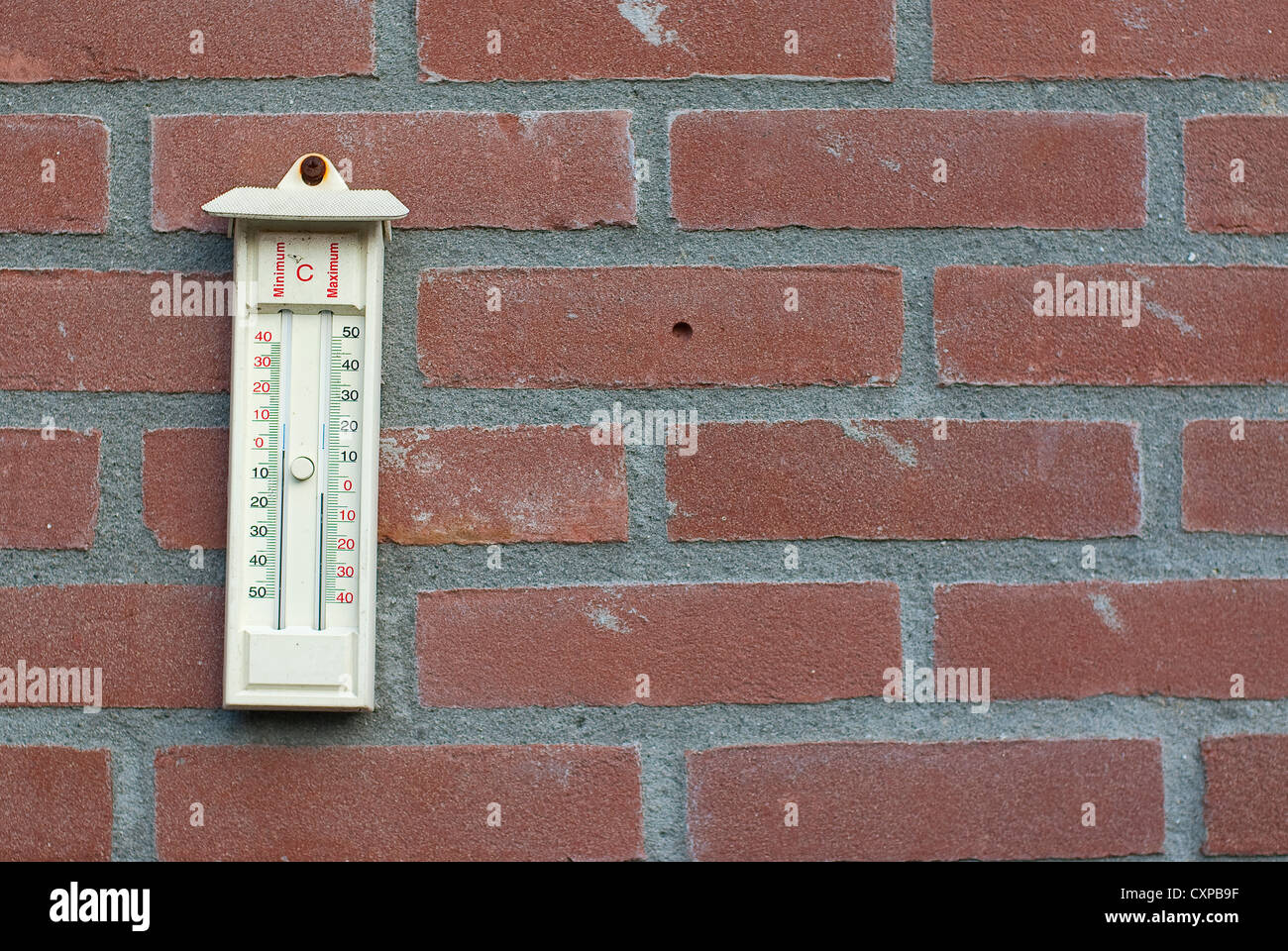 Thermometer hanging from a red brick wall showing the maximum and ...