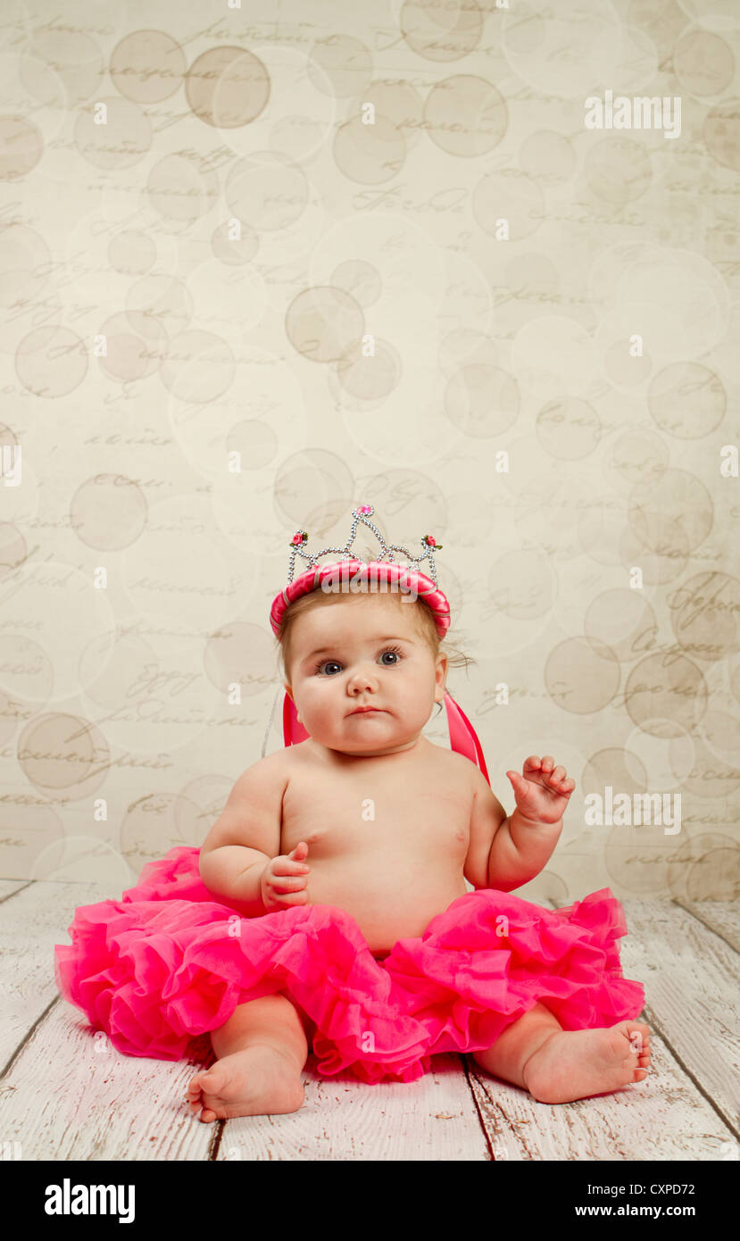 Pretty in a pink ruffled tutu a 6 month old baby girl wears a pink crown to match. Stock Photo