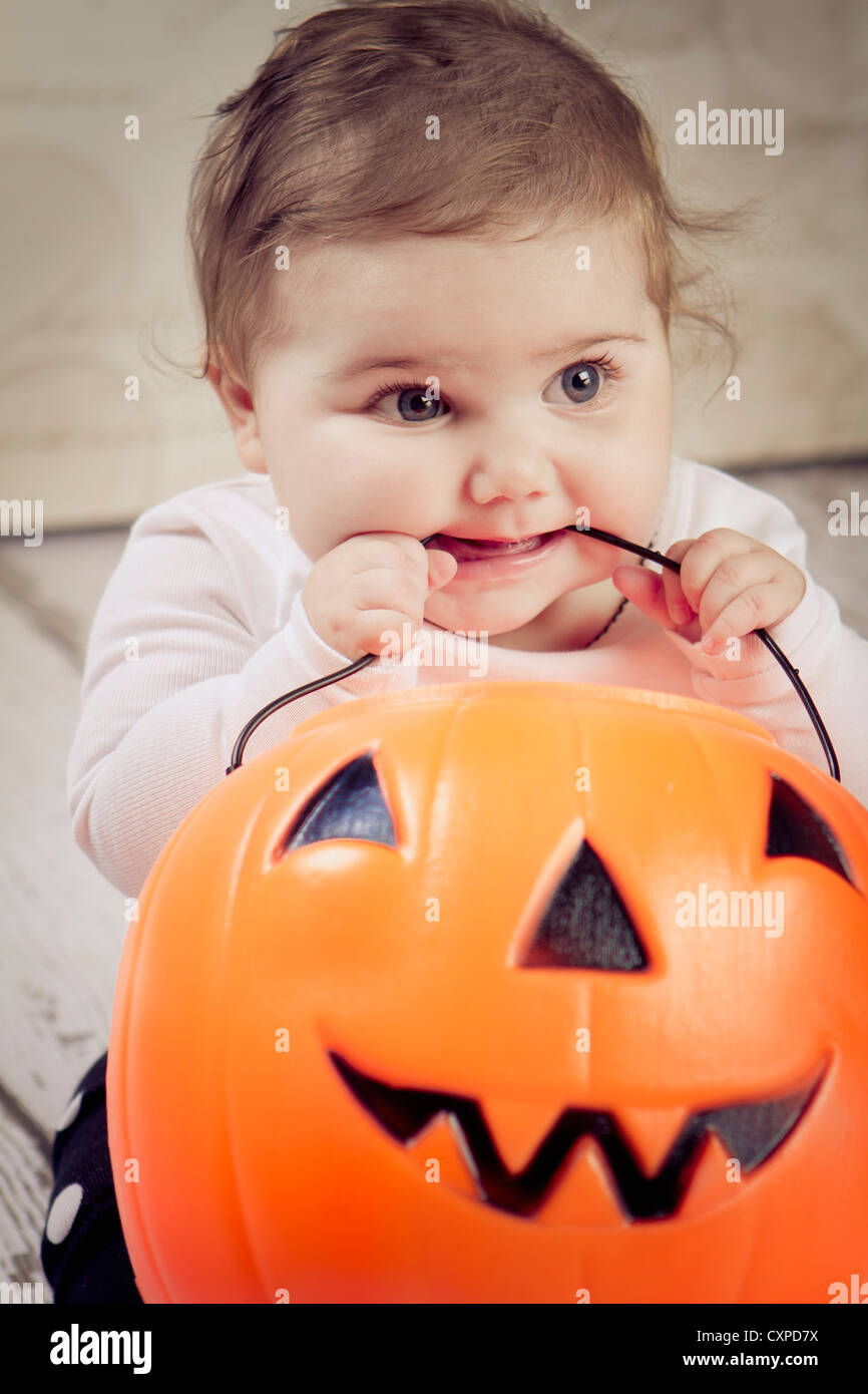 6 month old baby girl on her first Halloween chewing on the handle of her pumpkin used for trick or treating. Stock Photo