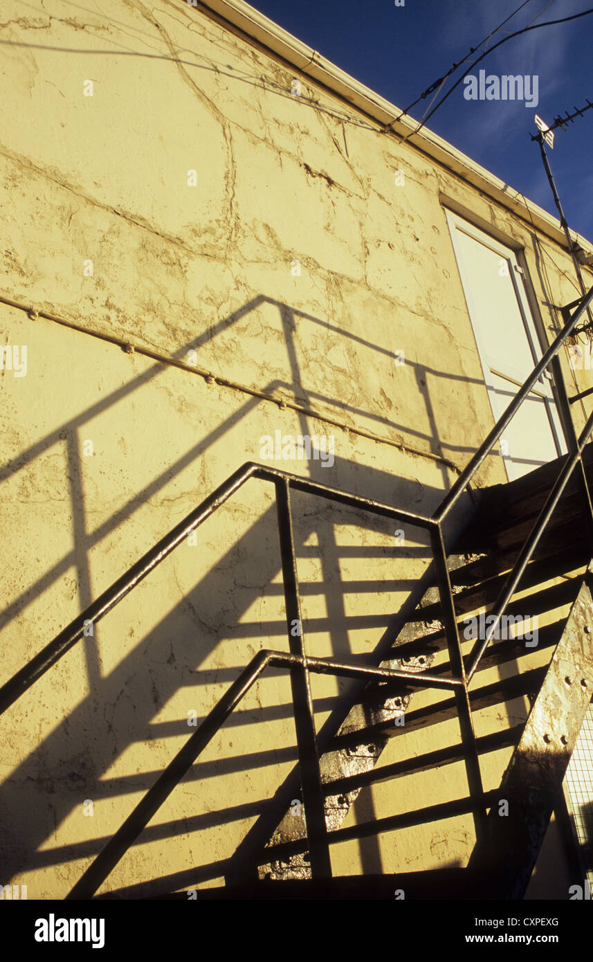 Detail of metal fire escape stairs casting shadows on pale wall in evening light Stock Photo