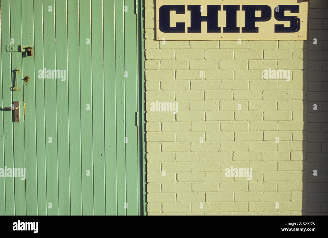 Padlocked wooden door set in white painted brick wall in warm light with sign stating Chips Stock Photo