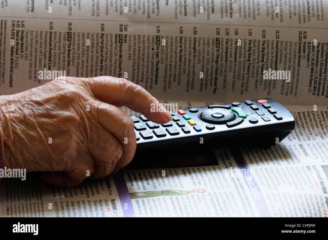 Elderly lady using a television remote control and a TV programme guide.  Senior using current technology. Stock Photo