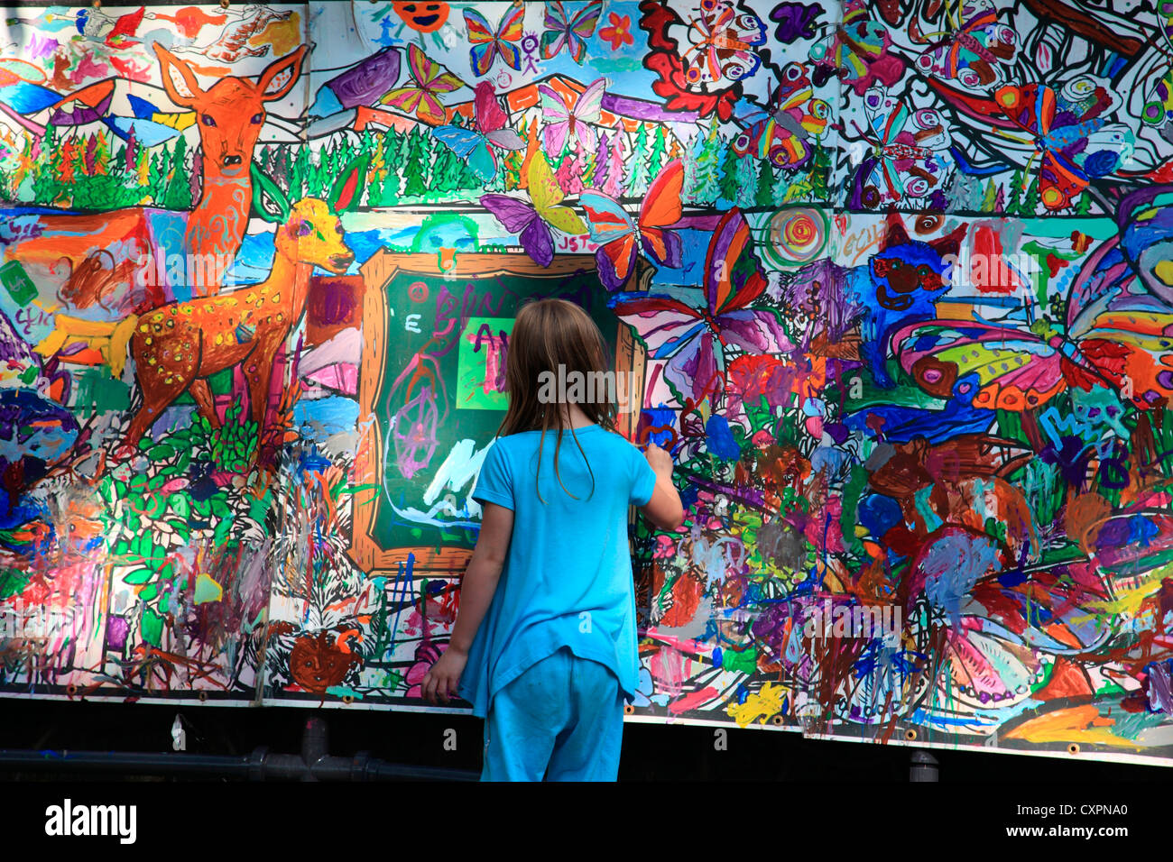Young girl standing in front of a large mural she is painting on at the ...