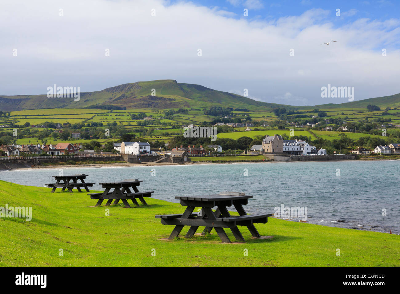 Picnic tables on seashore with view to village on north east coast route at Ballygally, County Antrim, Northern Ireland, UK Stock Photo