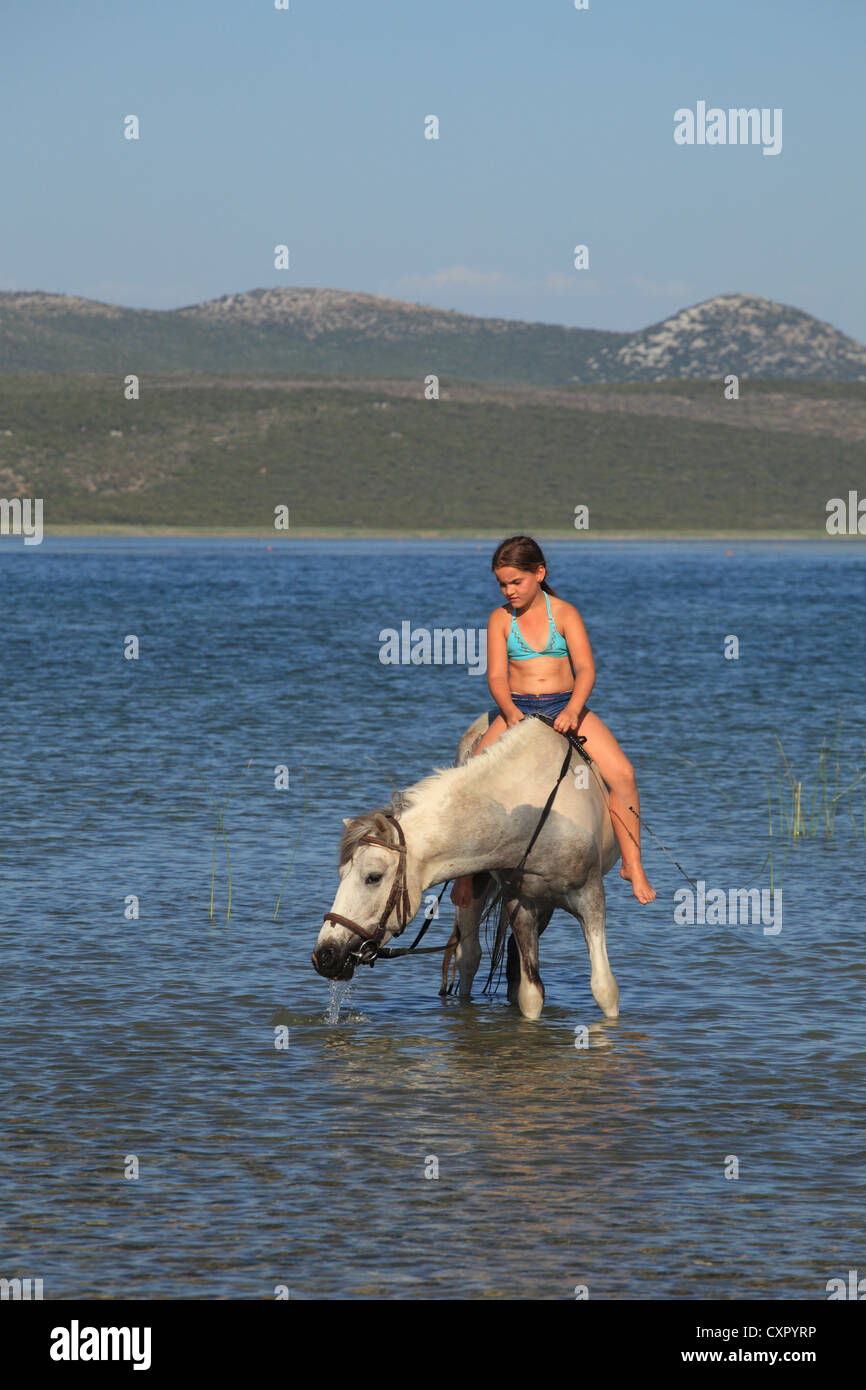 Girl riding a horse in the waters of Vransko jezero (Lake of Vrana) near Pakostane, Croatia. Stock Photo