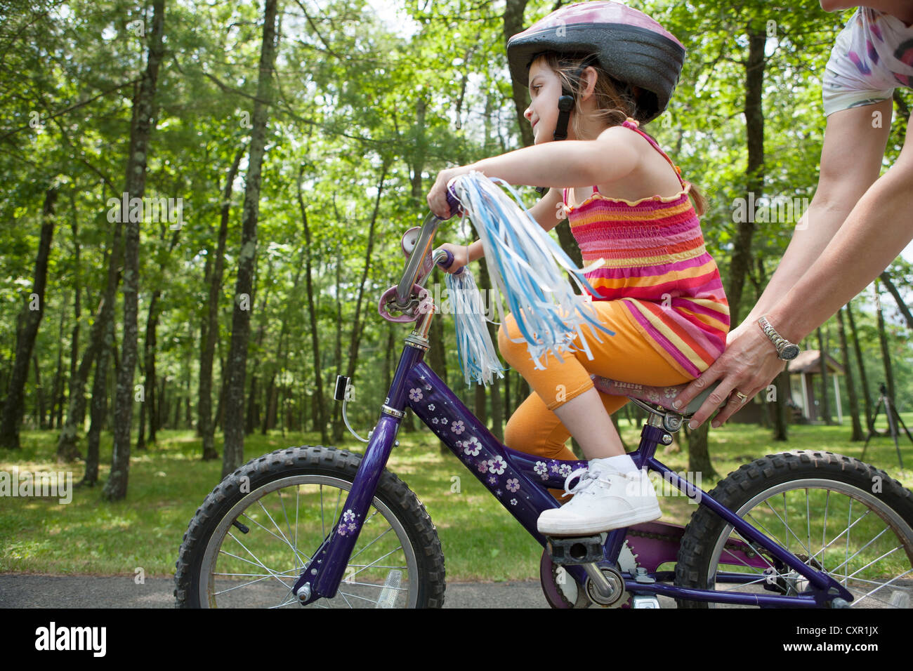 Mother helping daughter to ride bicycle Stock Photo