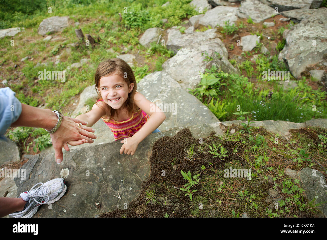 Mother helping daughter climb rocks Stock Photo