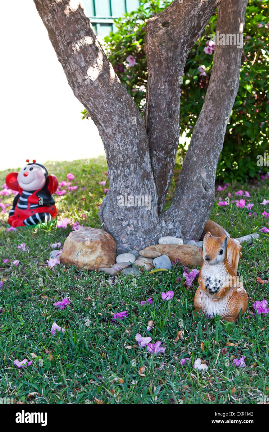 Two small decorative figures in the shape of a ladybug and squirrel, used as garden gnomes in the lawn under a tree Stock Photo