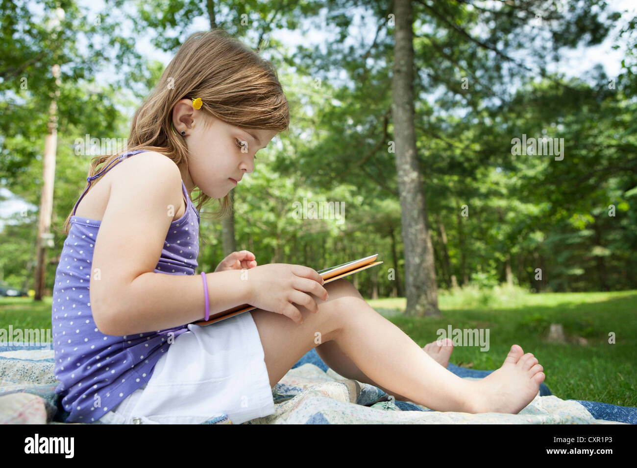 Girl sitting on picnic blanket with digital tablet Stock Photo