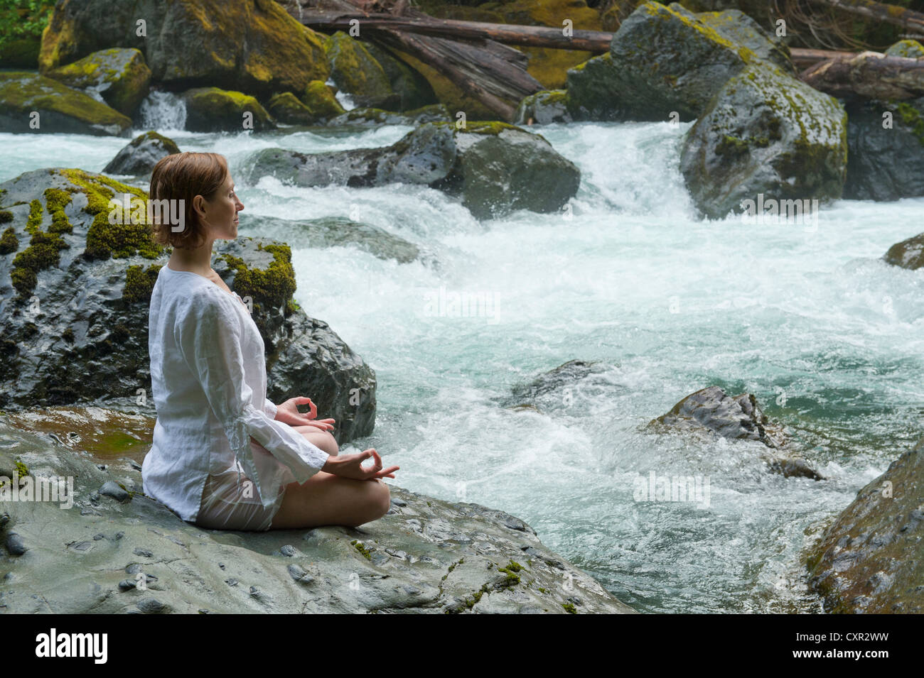 Woman meditating on rock by water Stock Photo