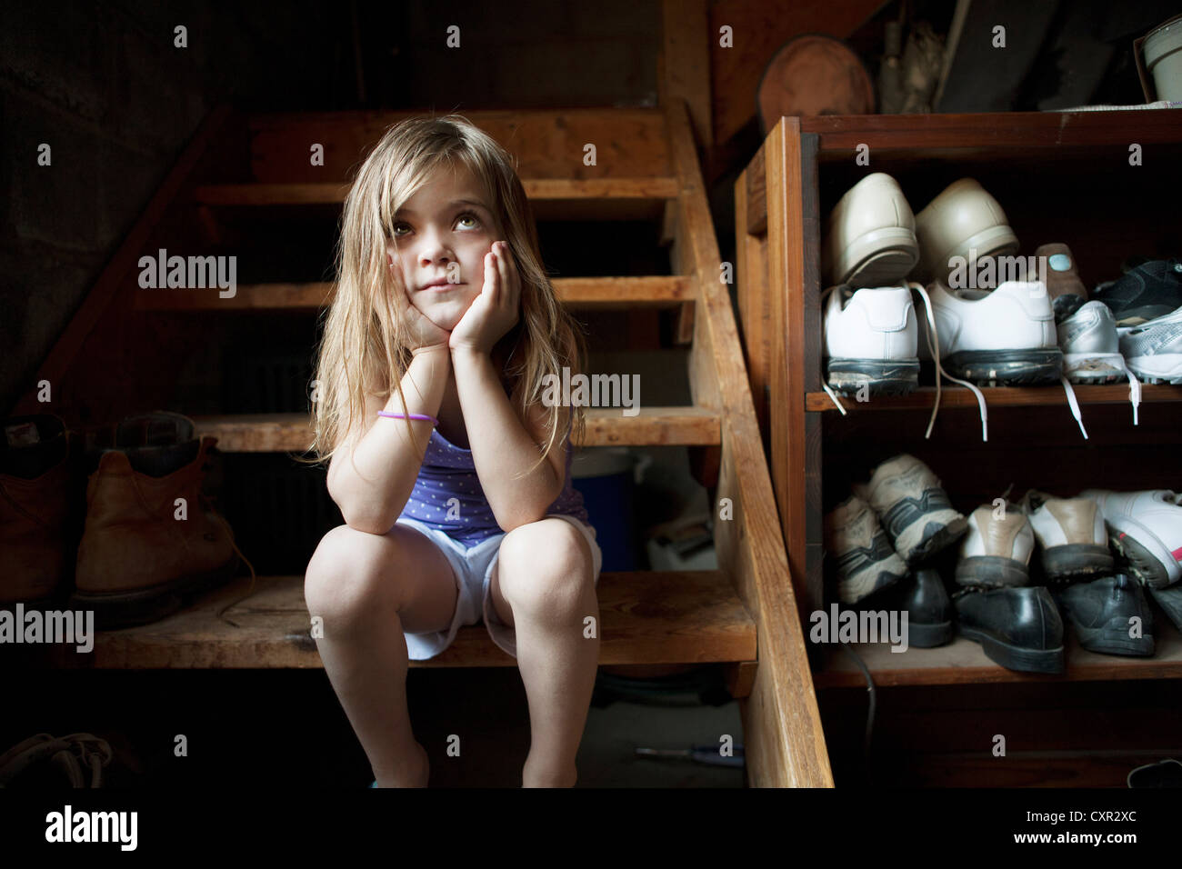 Little girl sitting on basement steps, looking up Stock Photo