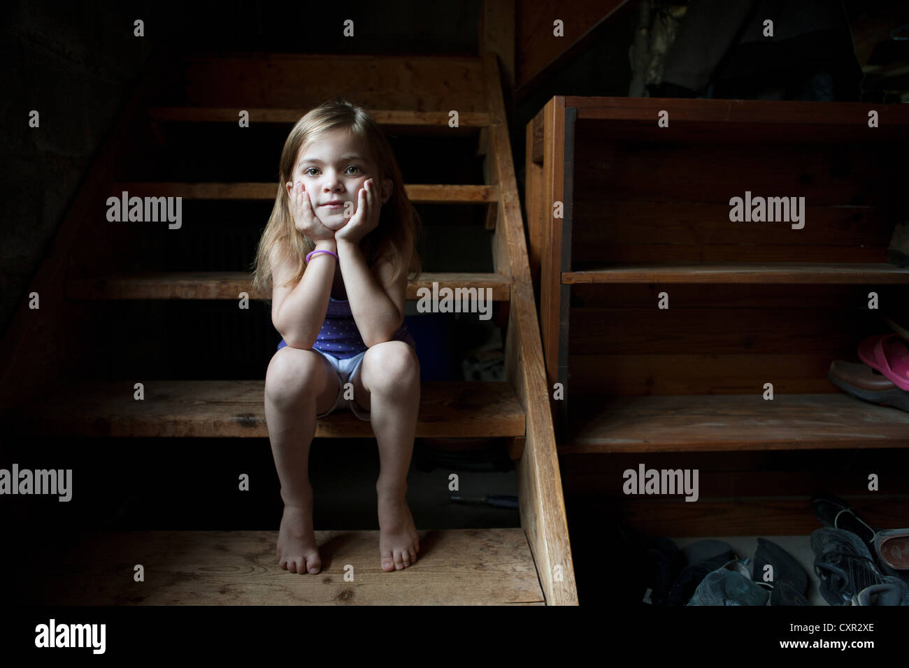 Little girl sitting on basement steps, looking at camera Stock Photo
