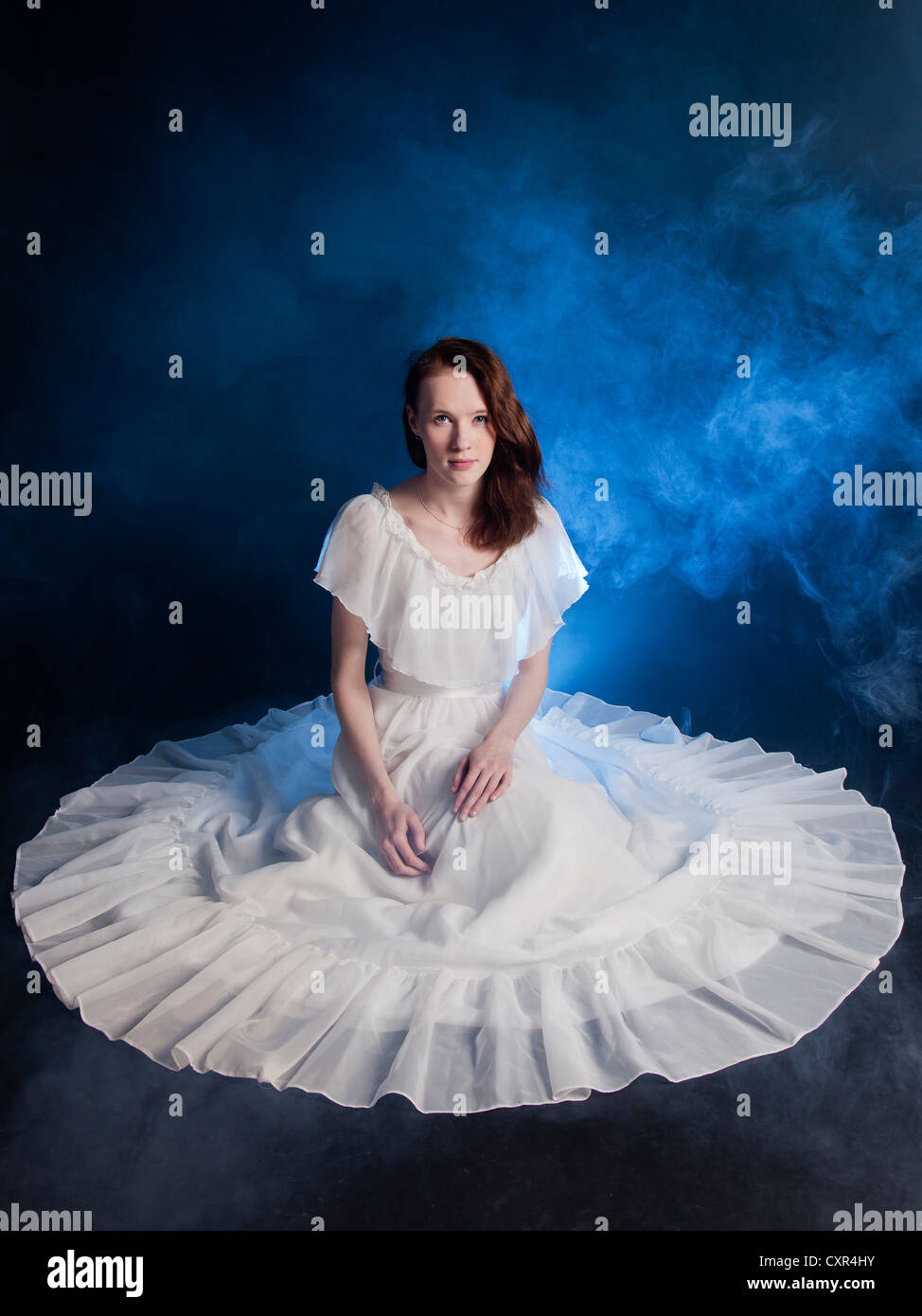 A young bride wearing wedding dress sitting on floor blue smoke around her. Stock Photo