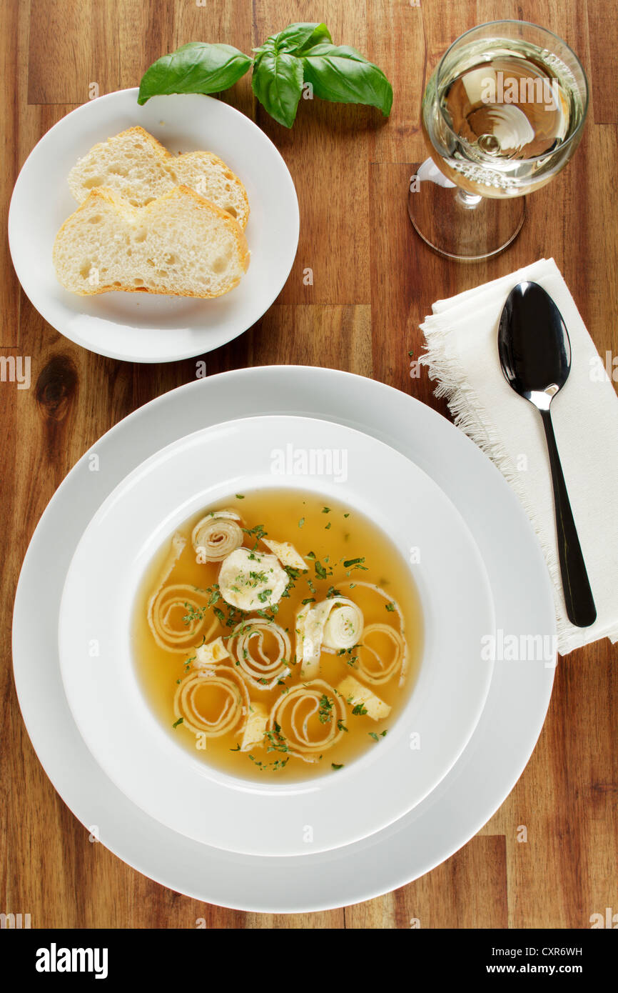 Wedding soup, beef stock with dumplings, sliced pancakes and egg served with white bread and white wine Stock Photo