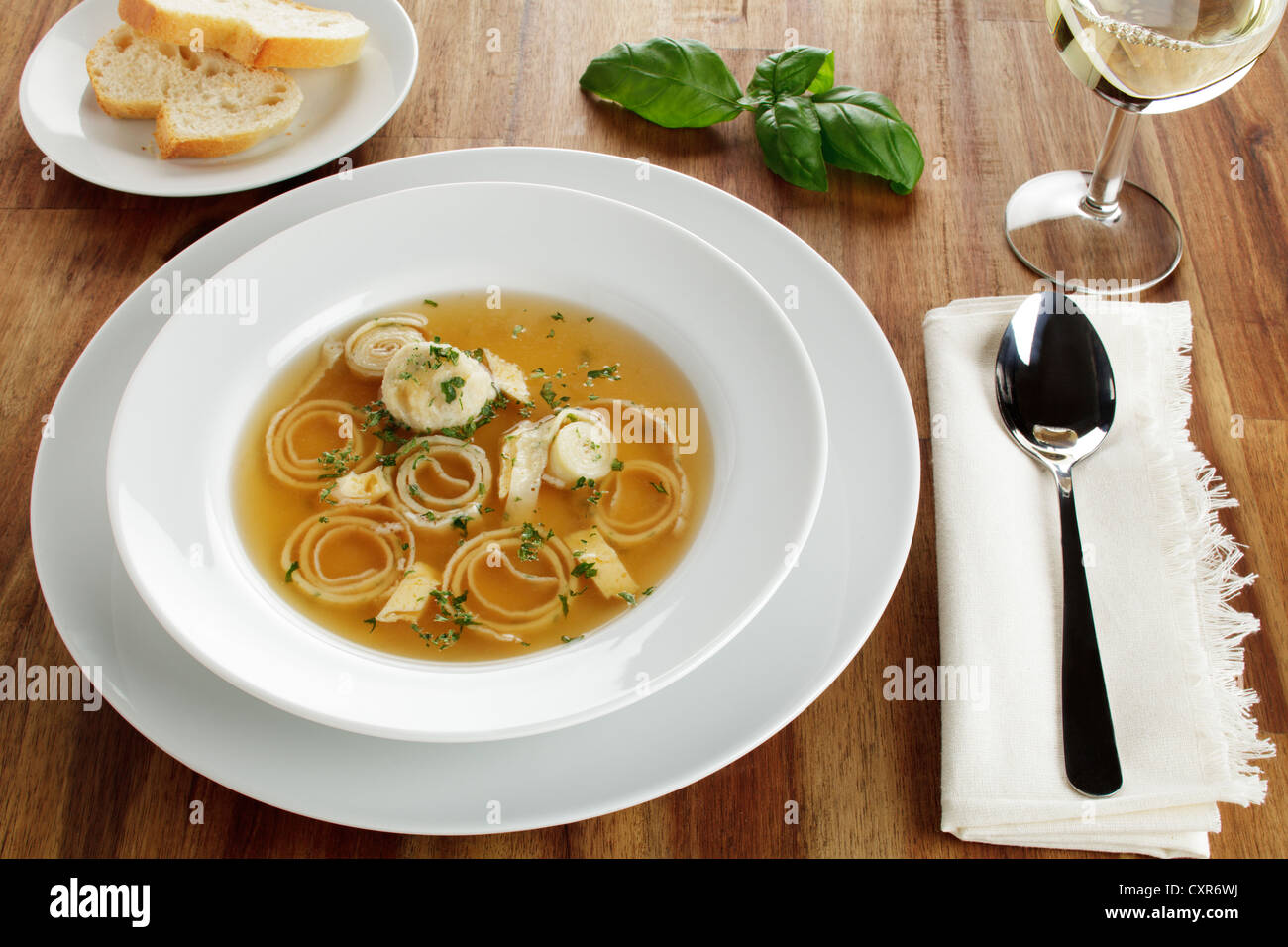 Wedding soup, beef stock with dumplings, sliced pancakes and egg served with white bread and white wine Stock Photo