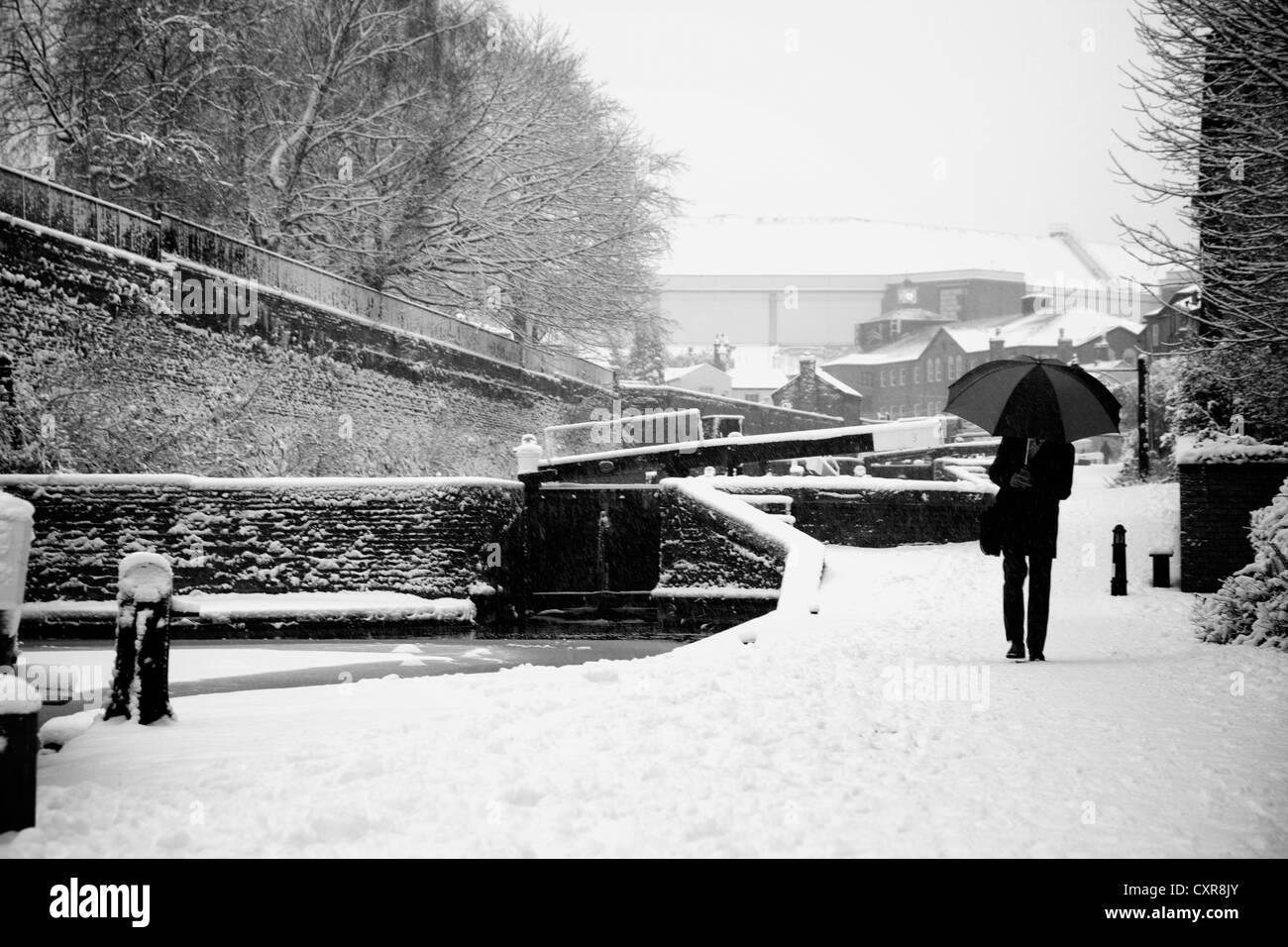 Man walking through the snow by canal in central Birmingham with umbrella on way to work, commuting Stock Photo