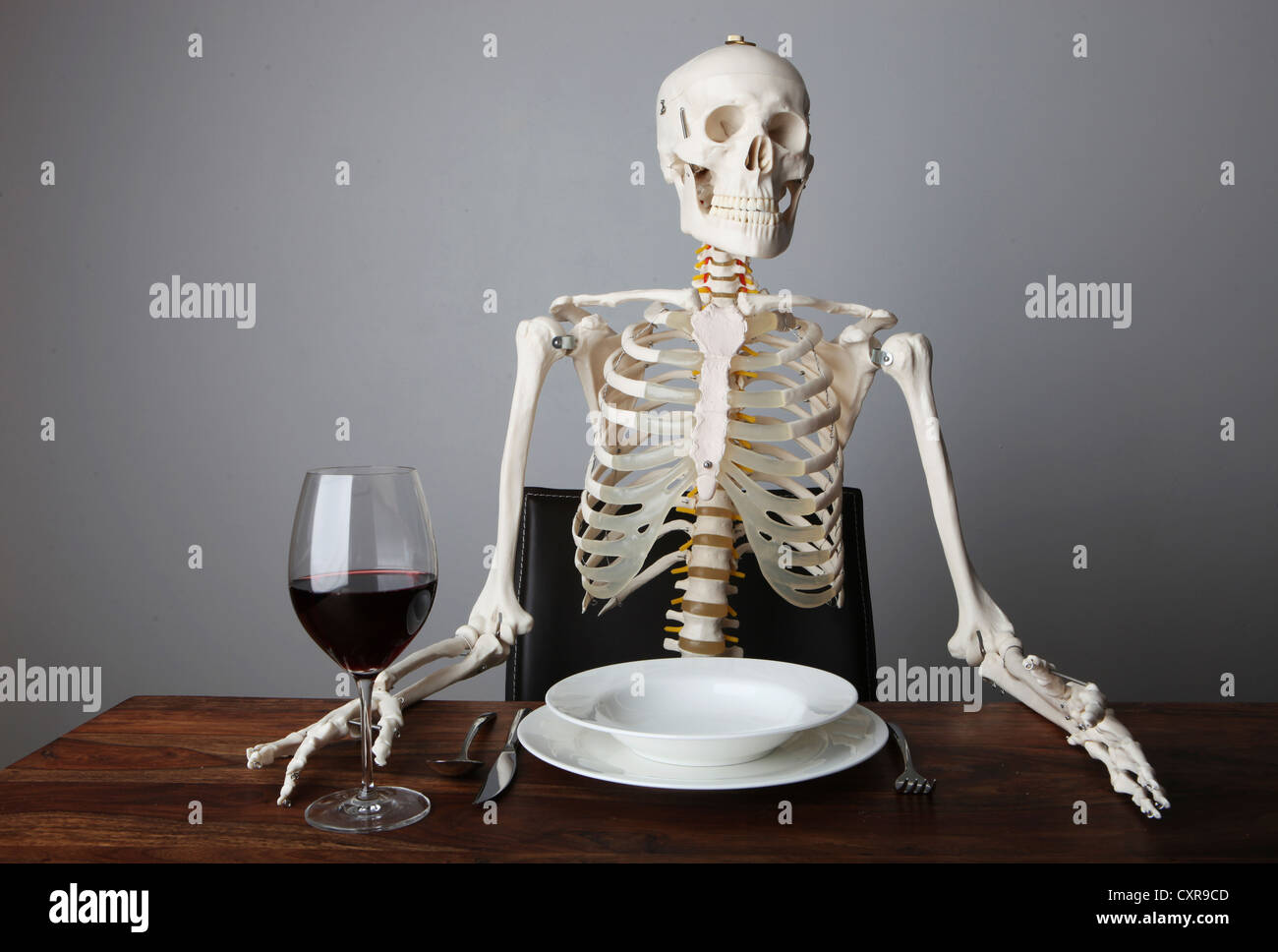 Skeleton sitting with a glass of red wine in its hand at a laid table Stock Photo