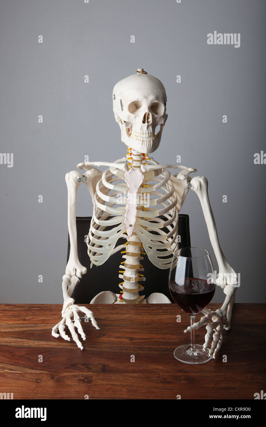 Skeleton holding a glass of red wine on a table Stock Photo