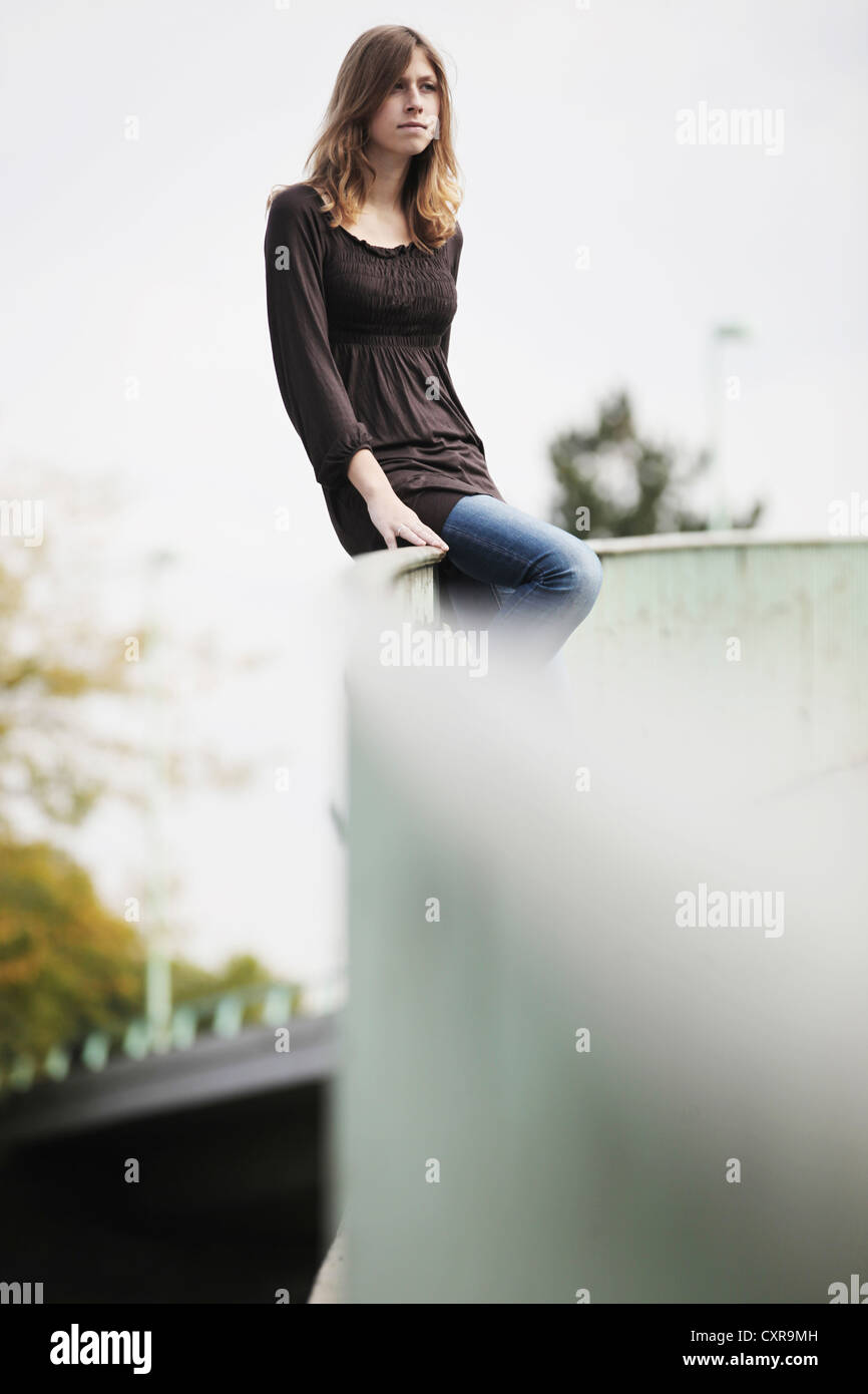 Young woman sitting on a railing, in an urban environment Stock Photo