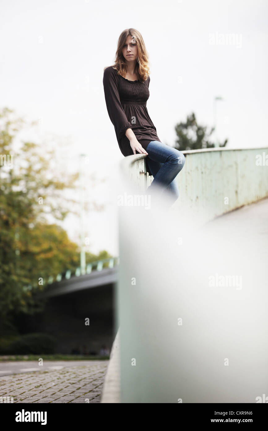 Young woman sitting on a railing, in an urban environment Stock Photo