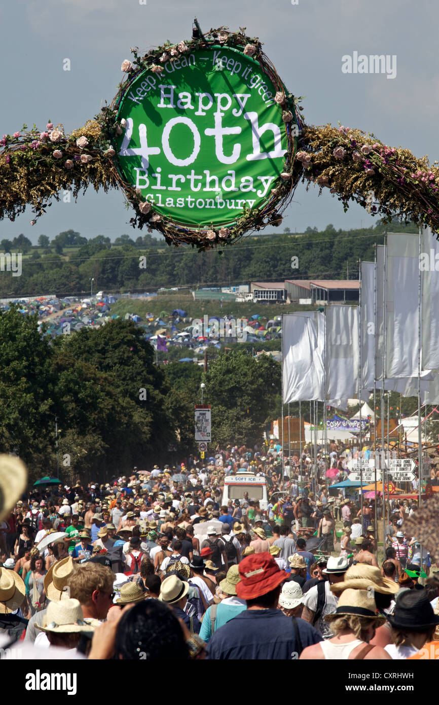 Crowds walk beneath a happy 40th birthday sign  in the sunshine at the Glastonbury Festival Stock Photo