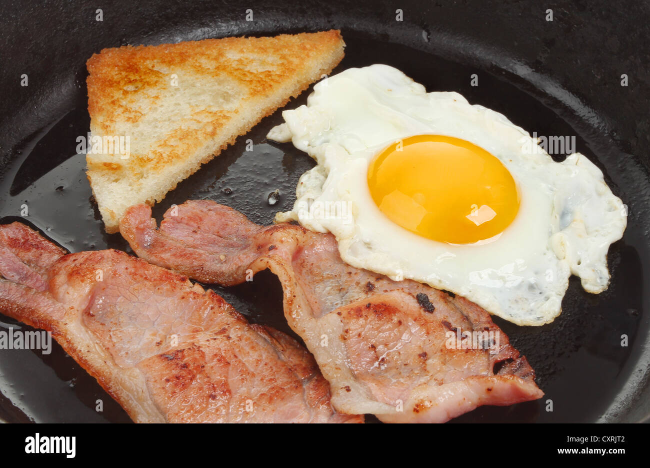Closeup of fried egg, bread and bacon in a frying pan Stock Photo