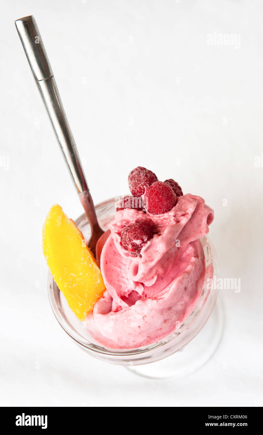 Raspberry frozen yogurt in a glass dish with a spoon and peach slice. Stock Photo