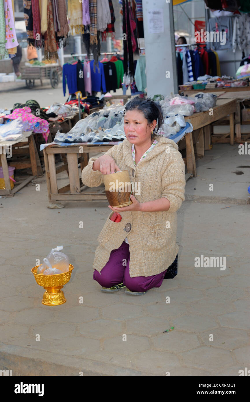 Buddhist shopkeeper waiting with offerings for the Buddhist mendicants in the early morning in the town of Phonsavan, Laos Stock Photo