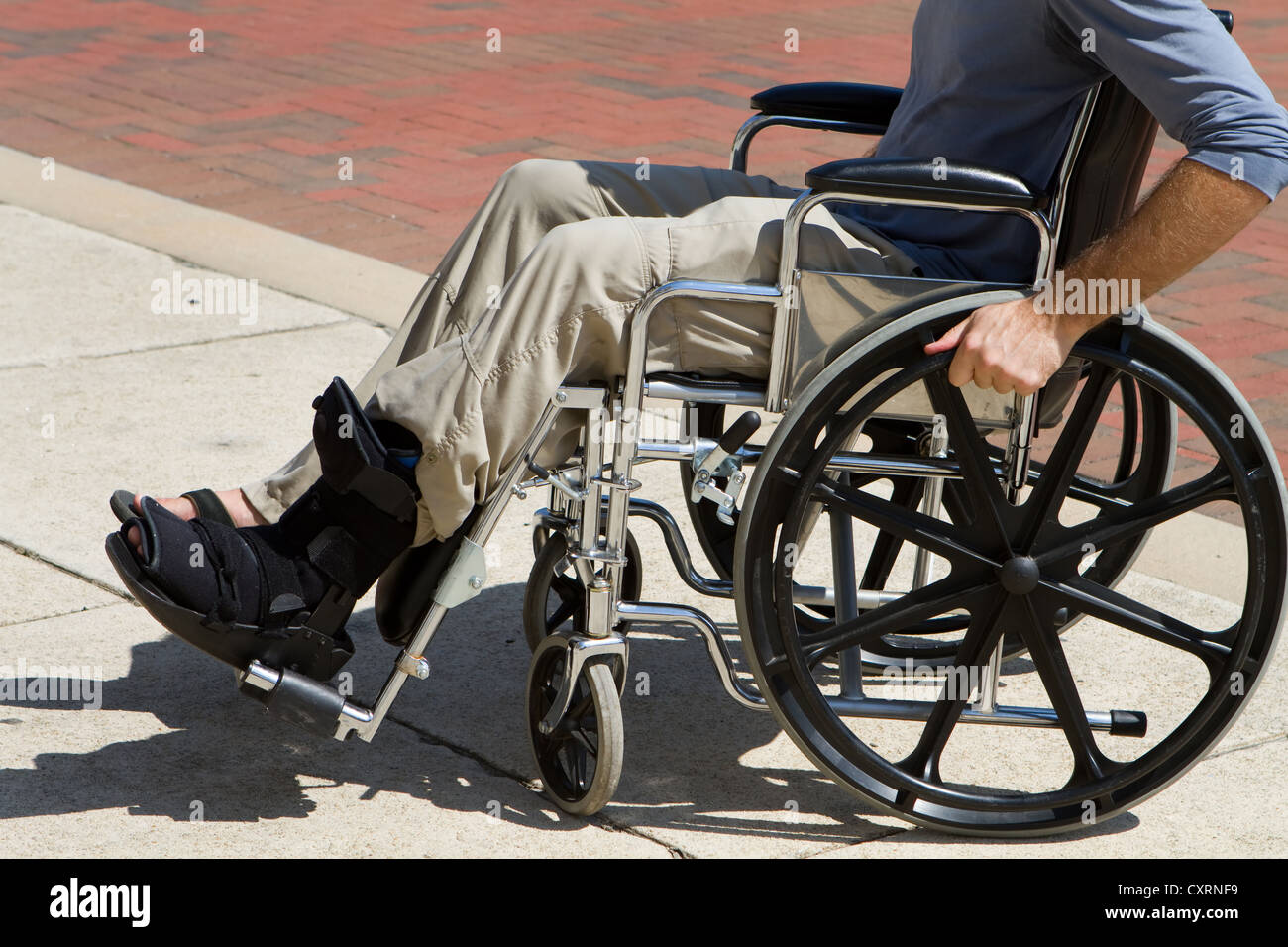 Injured man with a broken foot pushes himself along in his wheelchair. Stock Photo