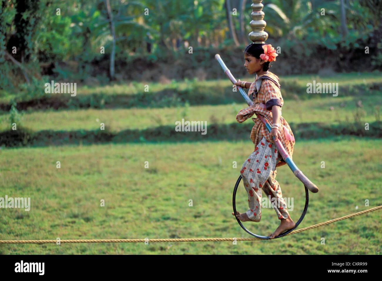 Girl balancing on a high wire on a bicycle wheel, village of