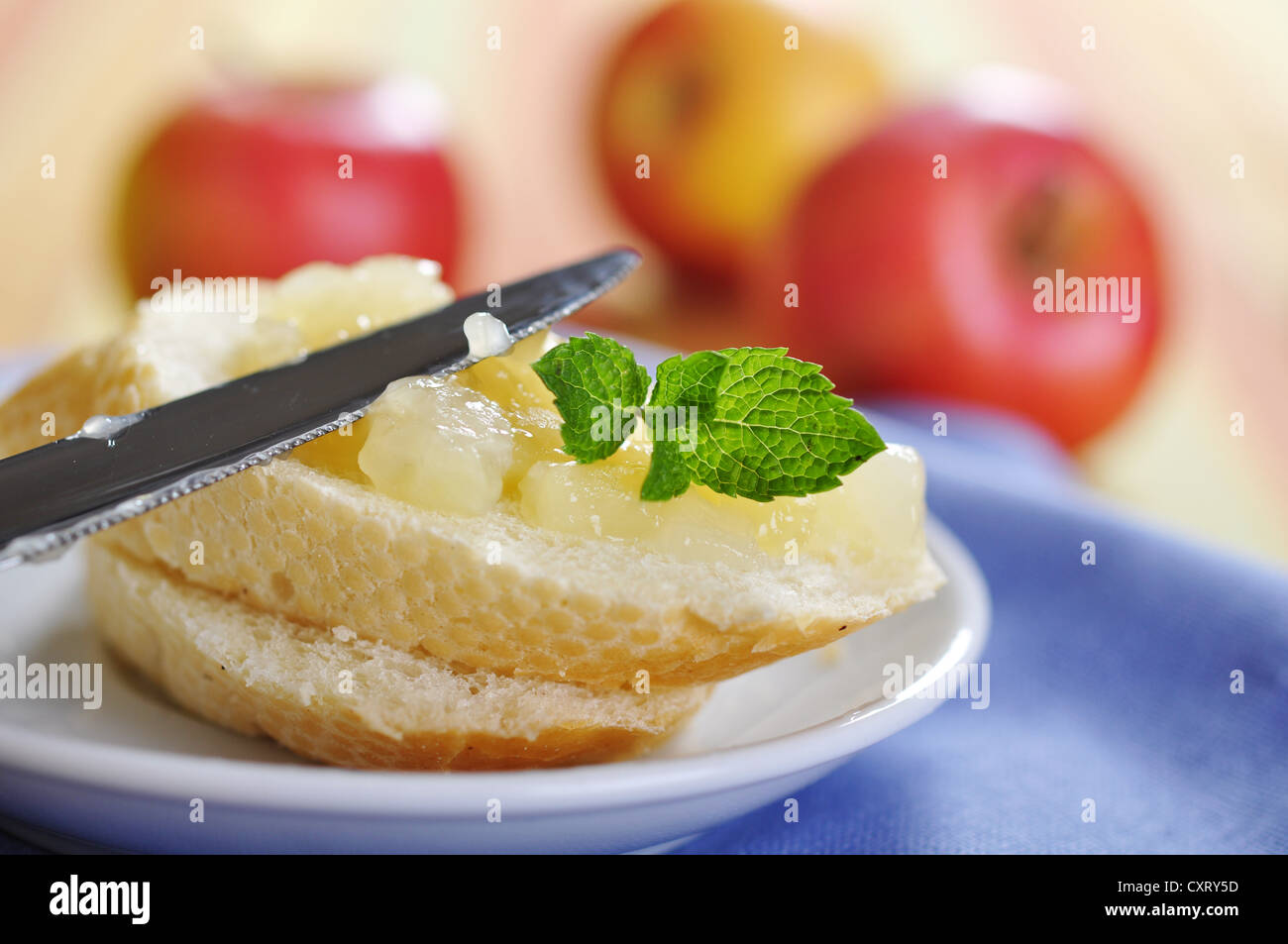 Sliced bun with apple jam and knife on plate. Small shallow dof. Stock Photo
