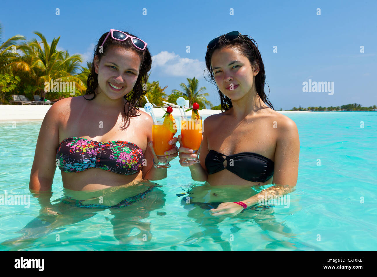 Two girls, about 14 and 18 years old, with sunglasses in their hair, drinking cocktails in a turquoise-coloured lagoon in the Stock Photo