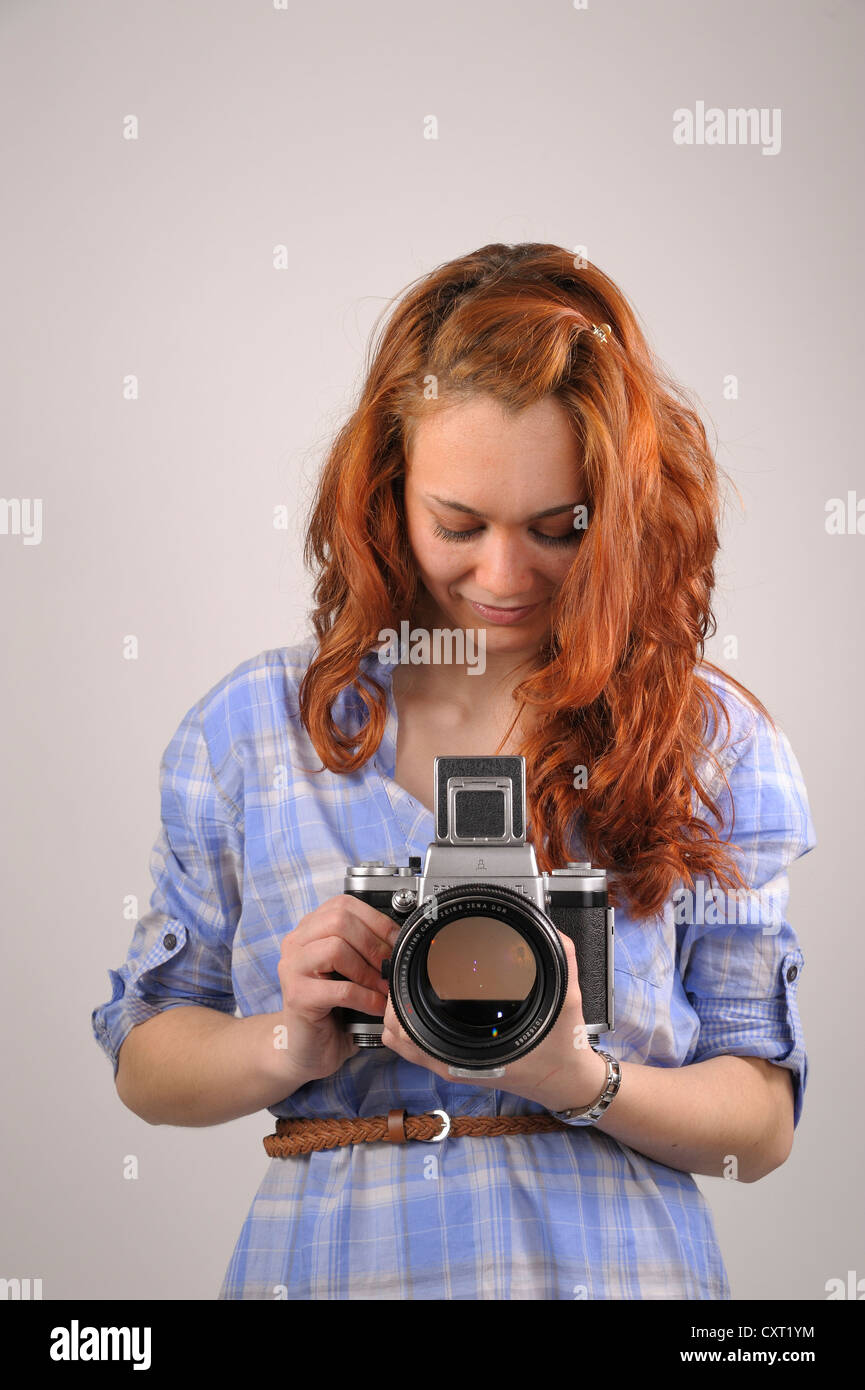 Young woman with red hair taking a photograph with an analog medium format camera Pentacon Six Stock Photo